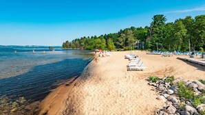 En strand med kristallklart blått vatten, en sandstrand och solstolar.