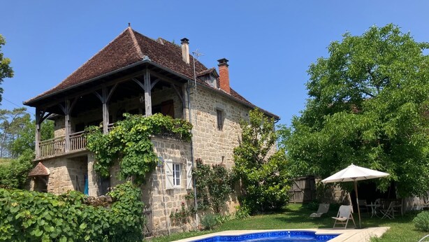 Une maison en pierre avec une piscine, entourée de verdure et sous un ciel dégagé.