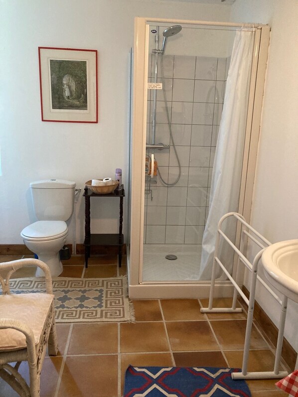 A bathroom with a toilet, a shower enclosure, a sink, and a framed picture on the wall.
