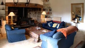 Ein gemütliches Wohnzimmer mit Kamin aus Stein, blauen Sofas und Holzbalken.