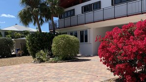 A two-story building with a balcony, a paved driveway, and a landscaped garden with red flowers. - Venetian Shores Escape! Heated Pool, 3BR, 70ft Dock, Dog-Friendly! (Islamorada)