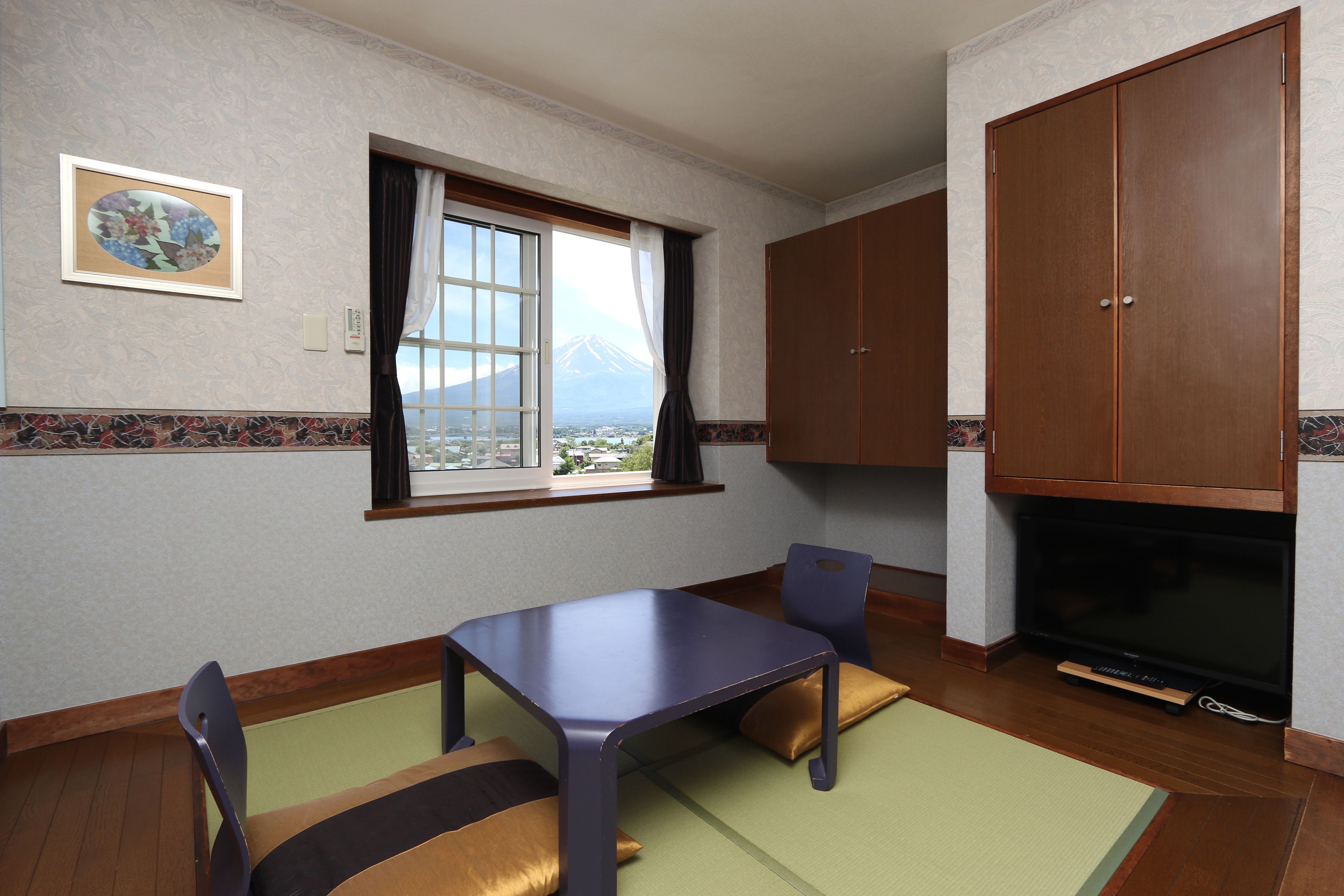 A room with a dining table, chairs, a television, and a view of a mountain through a window.