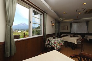 A dining area with tables and chairs, a view of a mountain, and a window with curtains.