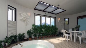 A sunlit indoor patio with a hot tub, potted plants, and a dining area. - Fujikawaguchiko Crescendo (Fujikawaguchiko)