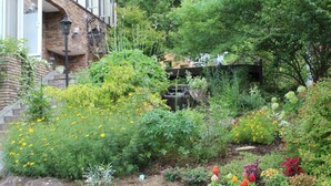 A garden with a variety of plants and flowers, a small waterfall, and a brick building with a staircase. - Fujikawaguchiko Crescendo (Fujikawaguchiko)