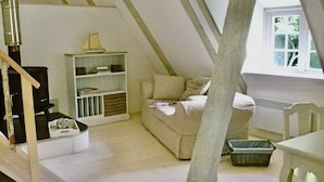 Una habitación estilo loft con techo alto, estantería empotrada, un sofá y una mesa de comedor.