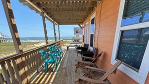 Une terrasse en bois avec des sièges extérieurs, offrant une vue sur une plage et l’océan.