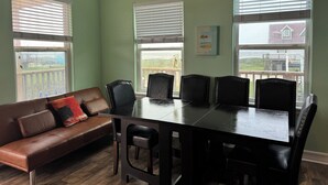 Un coin repas avec une table et des chaises, un canapé en cuir marron et de grandes fenêtres équipées de stores.