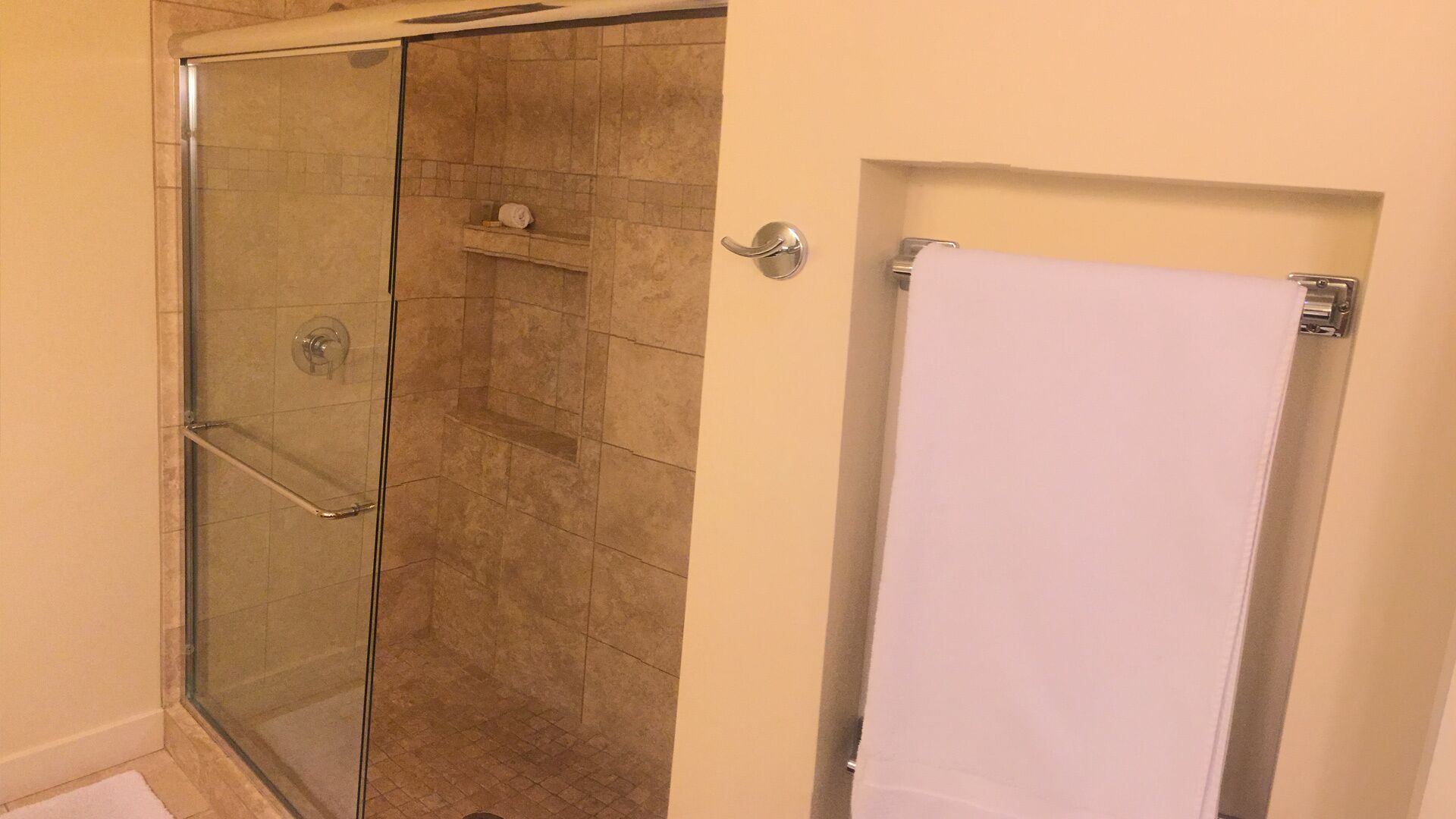 A glass-enclosed shower with a towel rack and a white towel hanging on a door.