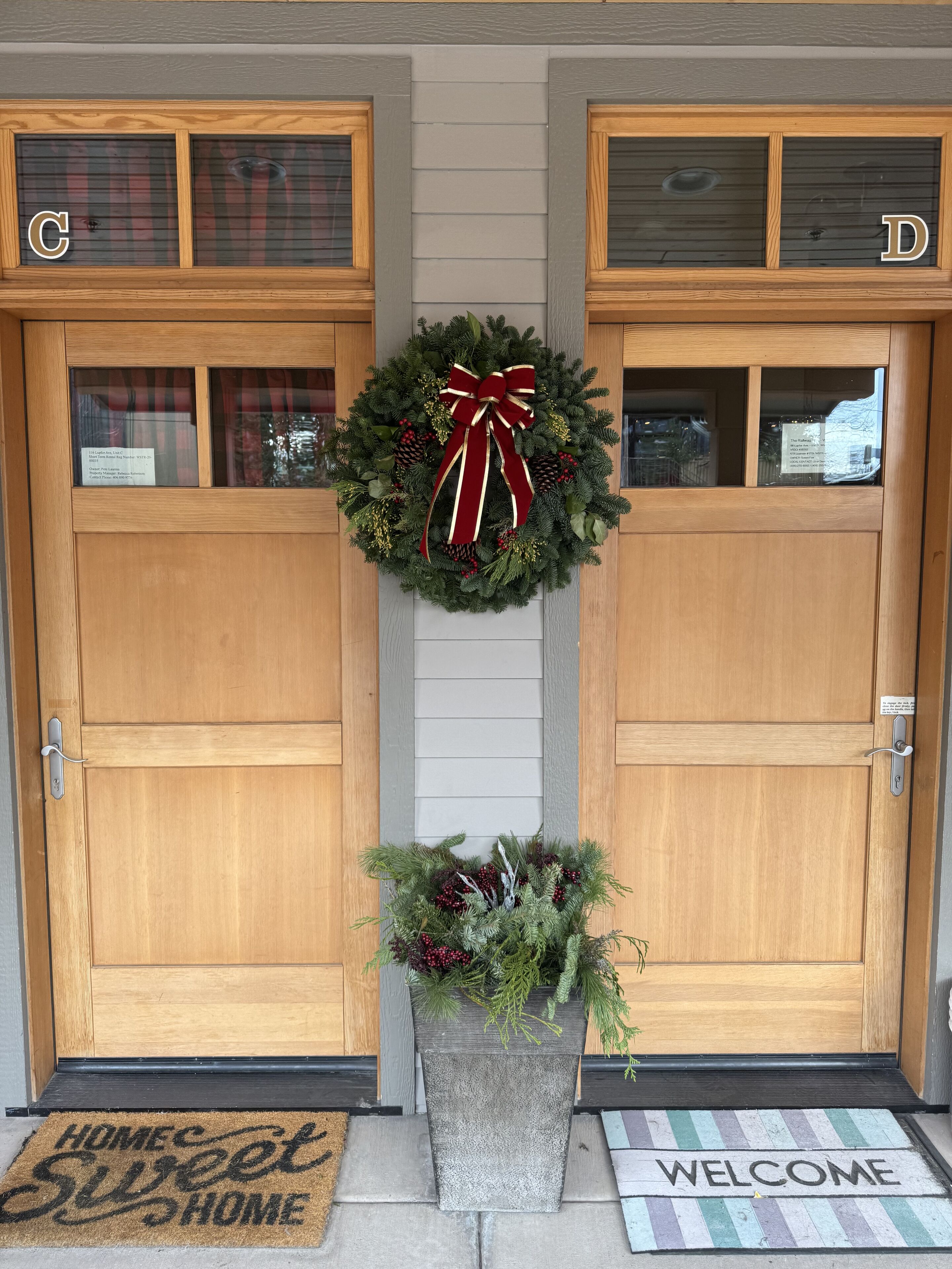A wooden double door with a wreath and a welcome mat.