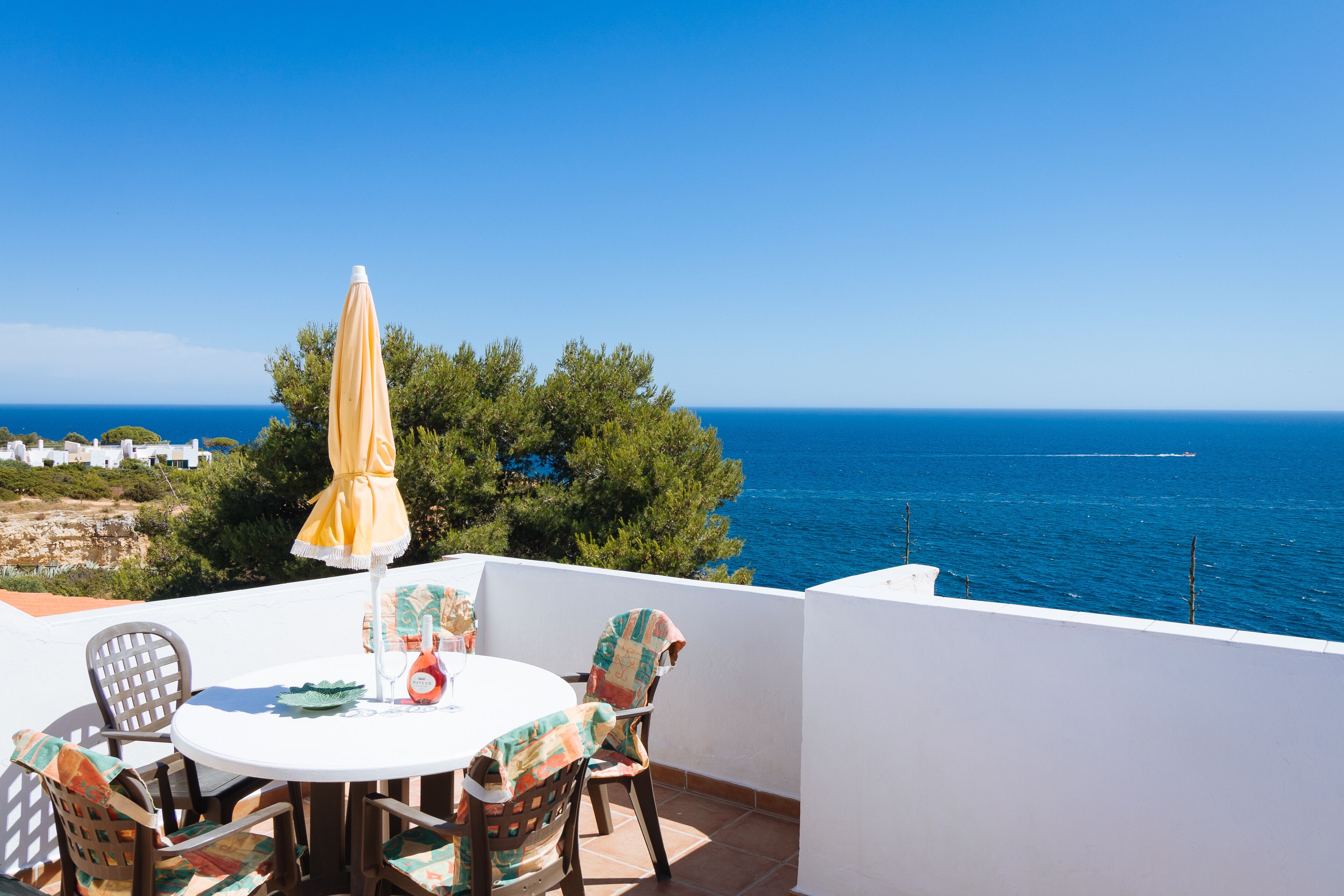 A terrace with a round table and chairs, a yellow umbrella, and a view of the sea.