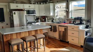 Una cocina moderna con armarios blancos, un refrigerador de acero inoxidable, una estufa a gas y una isla grande con taburetes de bar.