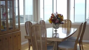 A dining area with a wooden table and chairs, a glass cabinet, and a vase of flowers. - Ocean View with 3 Master Suites in Roads End! (Lincoln City)