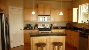 A kitchen with wooden cabinets, a central island with stools, a refrigerator, stove, and a dishwasher. - Ocean View with 3 Master Suites in Roads End! (Lincoln City)