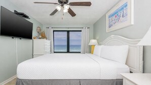 A bedroom with a bed, a ceiling fan, a TV, a dresser, a lamp, and a painting.