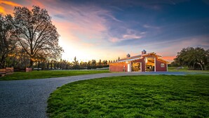 Ein rotes Bauernhaus mit einer großen offenen Tür, umgeben von einem gepflegten Rasen und einem Kiesweg, der dorthin führt.