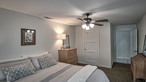 Ein Schlafzimmer mit Bett, Nachttisch, Kommode, Deckenventilator und einer Tür.