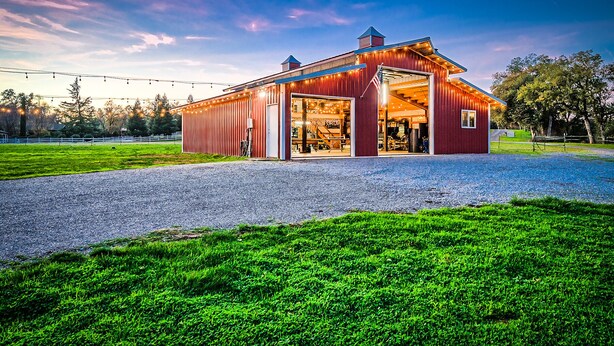 Ein rotes Bauernhaus mit geöffneten Türen, einer Schotterauffahrt und einem grünen Feld.