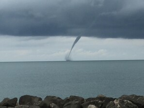 Une tornade se forme au-dessus d’une étendue d’eau, avec une côte rocheuse visible au premier plan.