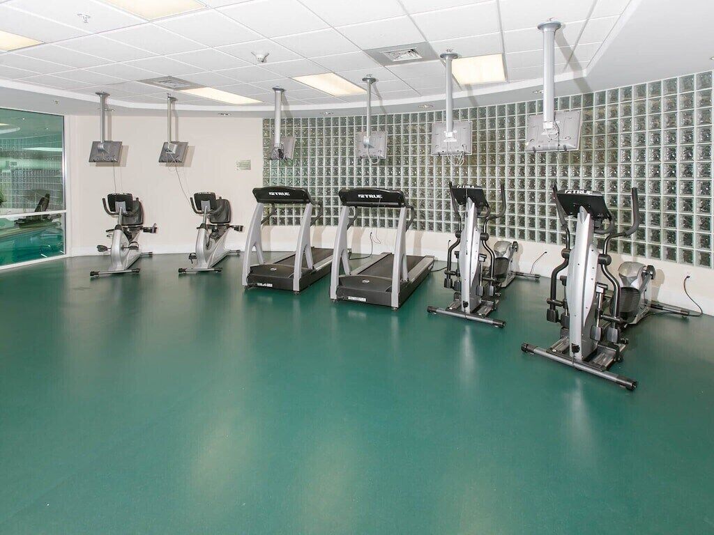A fitness room with treadmills, a green floor, and a wall with exercise equipment.