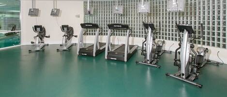 A fitness room with treadmills, a green floor, and a wall with exercise equipment.