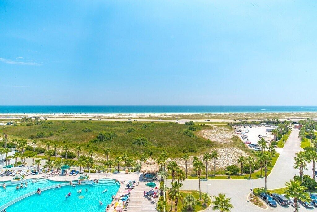 A resort with a large swimming pool, palm trees, and a beach view.