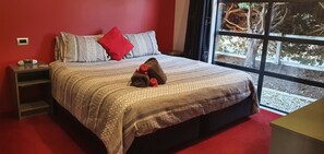 A neatly made bed with patterned bedding, a red pillow, and a pair of slippers on it.