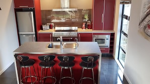 A modern kitchen with red cabinetry, a stainless steel stove, and a bar area with stools. - De Vine Martinborough 14a Cologne St (Martinborough)