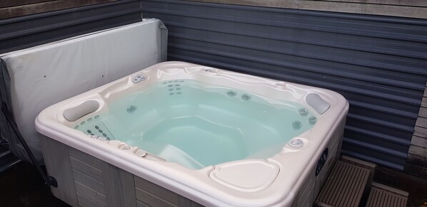 A hot tub with a control panel and a drain plug, placed next to a closed garage door.