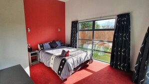 A bedroom with a large window, a red accent wall, and a bed with a patterned bedspread. - De Vine Martinborough 14a Cologne St (Martinborough)
