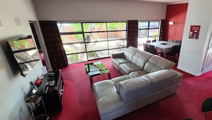 A living room with a red carpet, a white sofa, a glass coffee table, and a dining area with a table and chairs. - De Vine Martinborough 14a Cologne St (Martinborough)