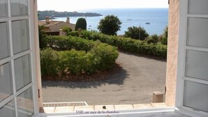 A view from a window overlooking a coastal area with a paved path, greenery, and boats on the water. - Villa 12 persons with heated swimming pool, sea view  (Saint-Raphaël)