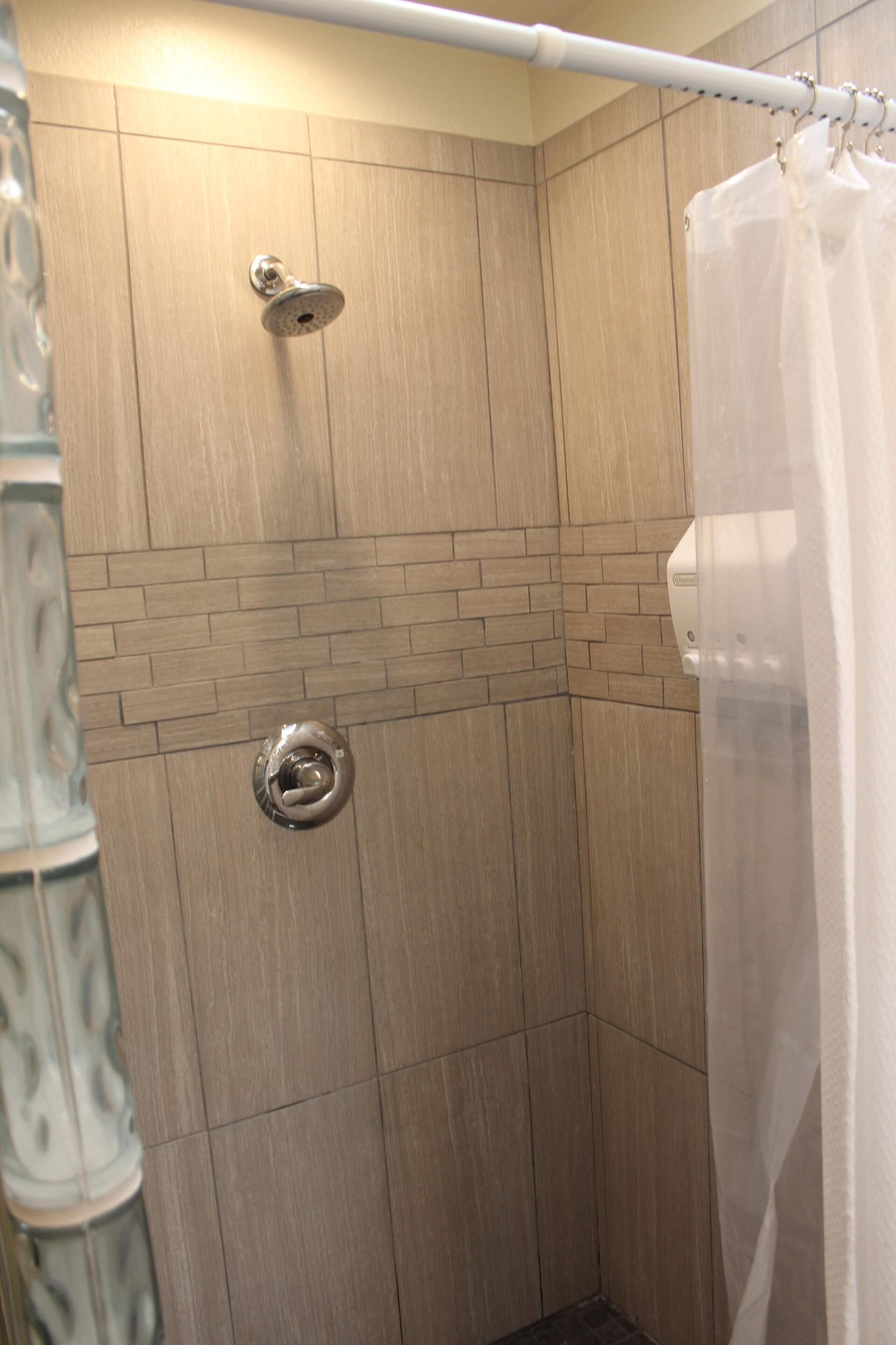 Una ducha con pared de azulejos, un cabezal y una cortina.