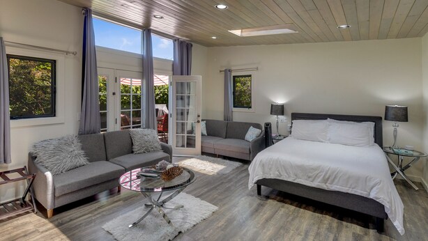 A modern bedroom with a large bed, two sofas, a glass coffee table, and a view of the outdoors.