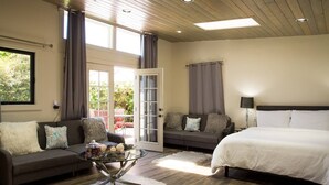 A bedroom with a large bed, two sofas, a glass coffee table, and a door leading to an outdoor area.