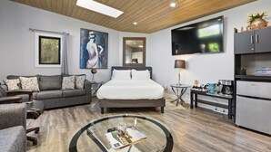 A modern bedroom with a bed, a sofa, a coffee table, a TV, and a kitchenette.