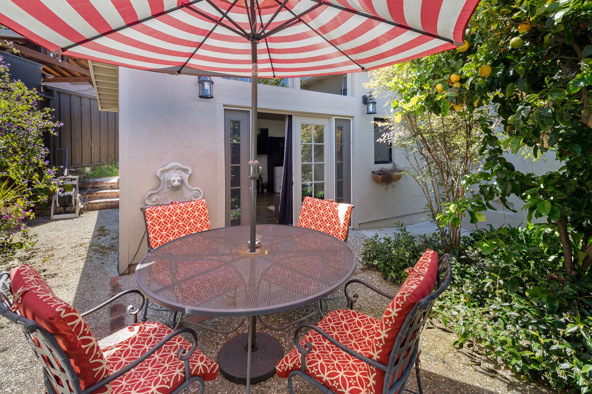 A round table with six chairs, each with a red and white patterned cushion, under a red and white striped umbrella.