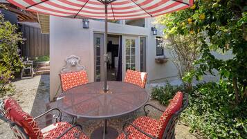 A round table with six chairs, each with a red and white patterned cushion, under a red and white striped umbrella.