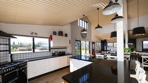 A modern kitchen with a large island, white cabinetry, and black countertops. - Abercrombie Ridge - Lux BARN and Spa Retreat - Pet-friendly (Curraweela)