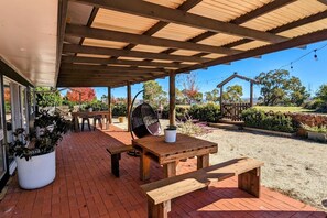 An outdoor patio area with a wooden table and benches, surrounded by potted plants and a gravel path. - Abercrombie Ridge - Lux BARN and Spa Retreat (Curraweela)
