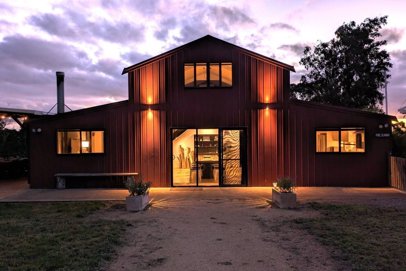 A two-story building with a large glass door entrance, a chimney, and a sign that reads 'THE BARN'.