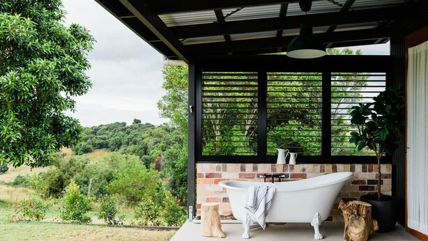 Une salle de bain avec une baignoire sur pieds, un mur en briques et une vue sur un paysage verdoyant.