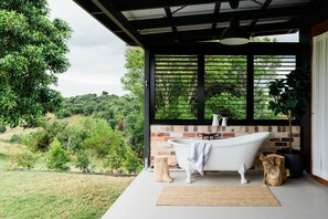 A bathroom with a freestanding bathtub, a brick wall, and a view of a lush green landscape.