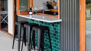 Une cuisine moderne dotée d’une grande fenêtre, de tabourets de bar et d’un comptoir agrémenté de verres et de bouteilles de vin.