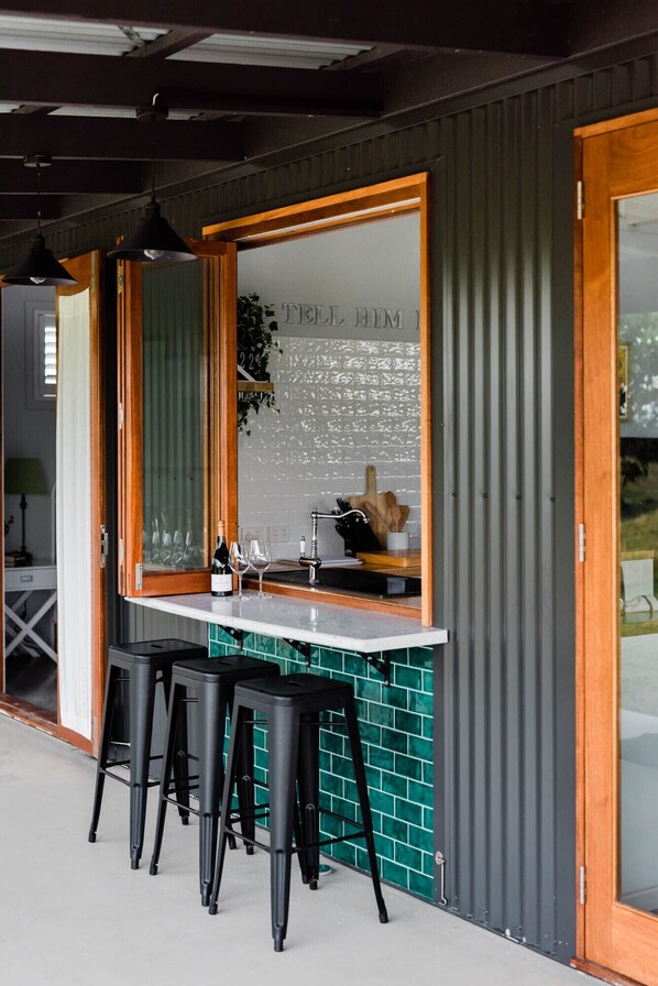 A modern kitchen with a large window, bar stools, and a counter with wine glasses and bottles.