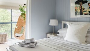 Une chambre à coucher avec un lit, un fauteuil suspendu, une table de chevet avec une lampe et une fenêtre donnant sur un paysage verdoyant.