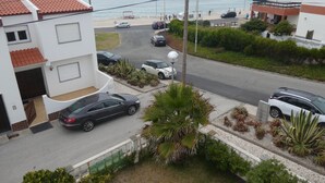 Une rue résidentielle bordée de voitures garées, un bâtiment blanc avec un toit recouvert de tuiles rouges, et une vue sur la mer.