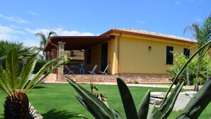 A yellow house with a stone foundation, a covered patio with chairs, and a well-maintained lawn. - Mediterranean villa - 150 meters from the promenade of Cefalu (Campofelice di Roccella (Pa))