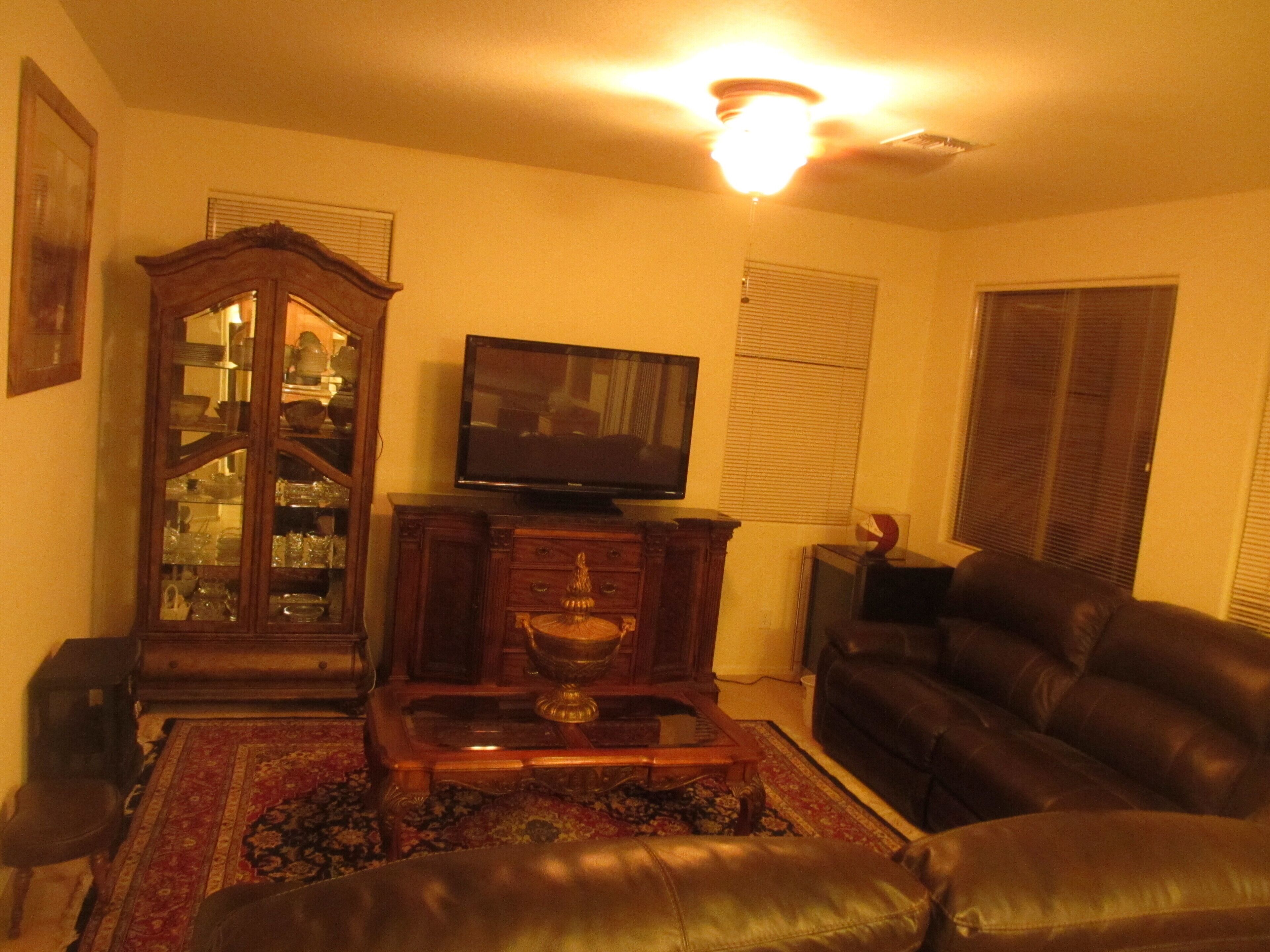 A living room with a television, a wooden cabinet, a leather sofa, and a patterned rug.