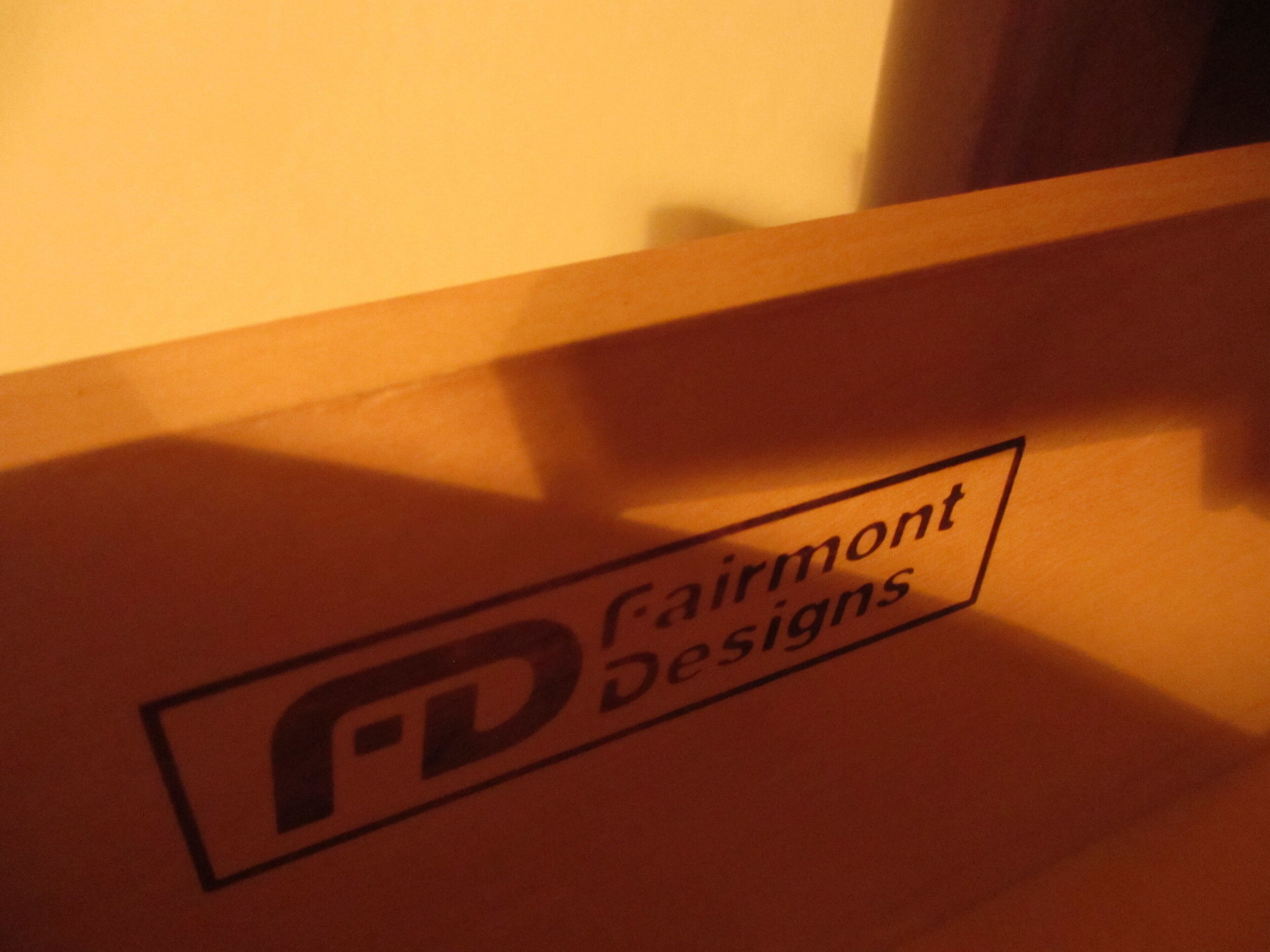 A logo with the text "Fairmont Designs" on a wooden surface.